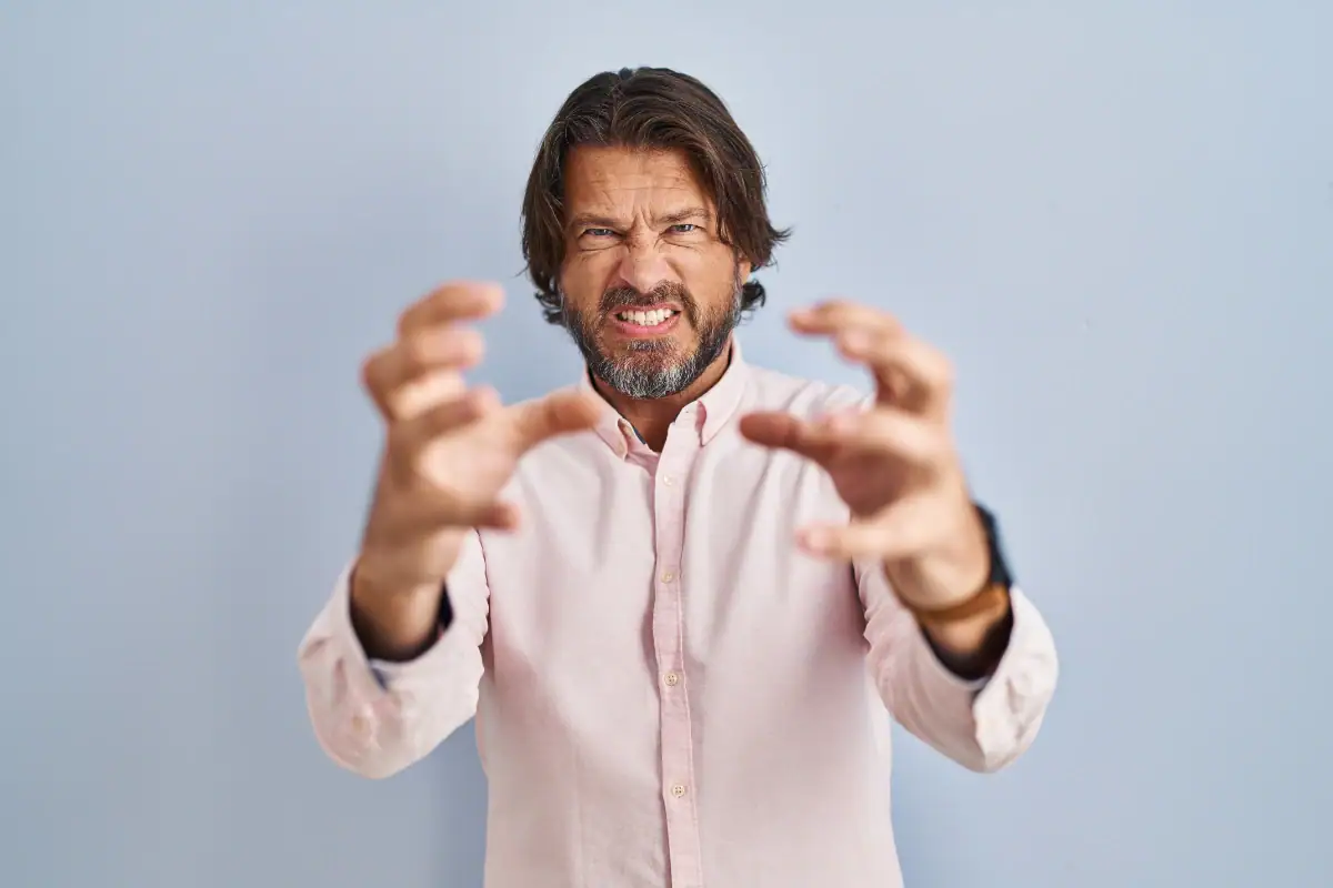 knappe man van middelbare leeftijd met een elegante shirtachtergrond die gefrustreerd schreeuwt van woedehanden die boos proberen te wurgen